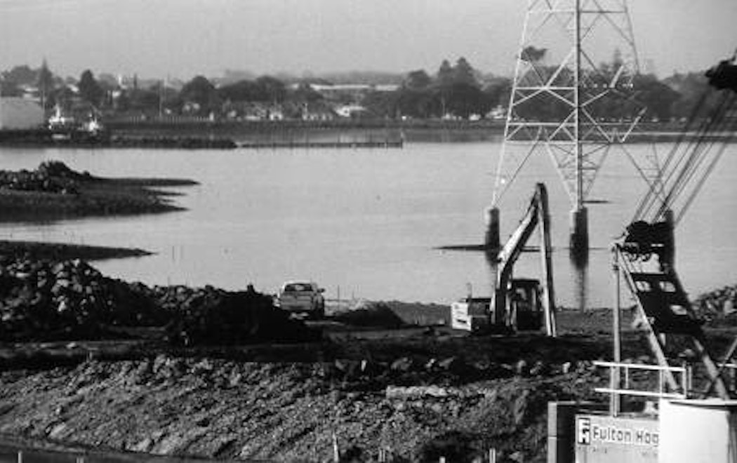 A digger operates near a power tower in the water